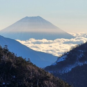 Uma imagem do Monte Fuji no Japão visto do alto de uma montanha. Há outras montanhas e nuvens. Vista panorâmica do Monte Fuji e outras montanhas do Japão de um cume com nuvens, representando a experiência de montanhismo e escalada com guia no Japão.